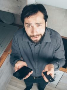 A confused man indoors looks up while holding a smartphone and credit card, concerned about a data issue.